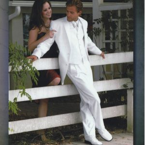 Man wearing white tuxedo leaning against a fence